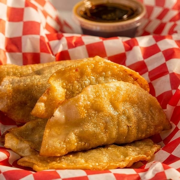 Golden-brown fried dumplings in a red and white checkered paper-lined basket with a side of sauce.