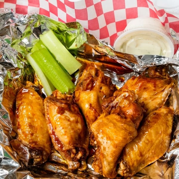 Glazed chicken wings with celery sticks and ranch dip in a takeout container.