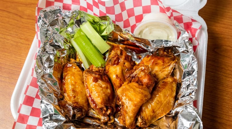 Glazed chicken wings with celery sticks and ranch dressing in a takeout container.