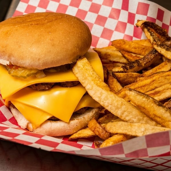 Cheeseburger with pickles and onions, served with a side of fries in a red and white checkered basket.