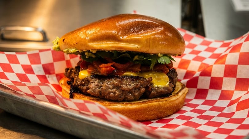 A juicy burger with melted cheese, guacamole, and red peppers on a brioche bun.