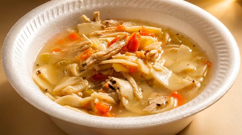 Chicken noodle soup with carrots and celery in a white styrofoam bowl.