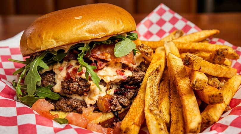 Double patty burger with bacon, arugula, cheese sauce, and tomatoes, served with fries.